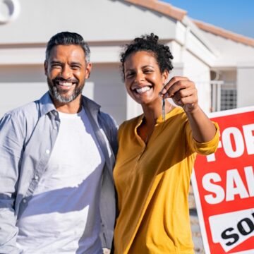 Happy couple buying a house A couple stands outside a home they just bought, with a woman holding keys