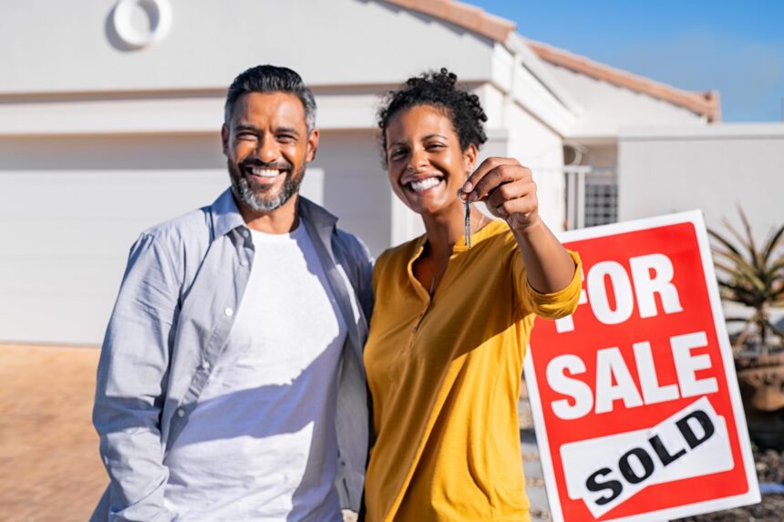 Happy couple buying a house A couple stands outside a home they just bought, with a woman holding keys