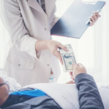 sick-businessman-are-working-on-hospital-bed-with-2025-03-26-09-00-09-utc A man pays a medical bill with cash while laying in a hospital bed