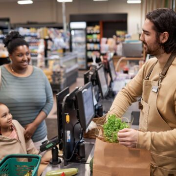 smiling-male-worker-in-supermarket-helping-young-w-2025-03-05-11-32-27-utc A woman checks out at a grocery store with her daughter