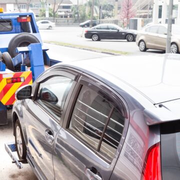 Tow truck towing a broken down car on the street. A car being towed