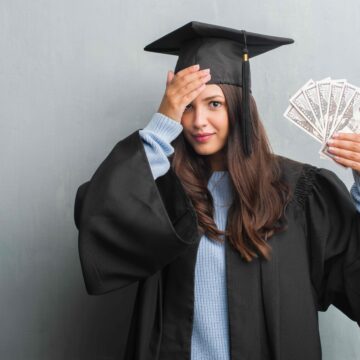 young-brunette-woman-over-grunge-grey-wall-wearing-2025-10-13-06-51-05-utc A woman in graduation robes looks stressed about money