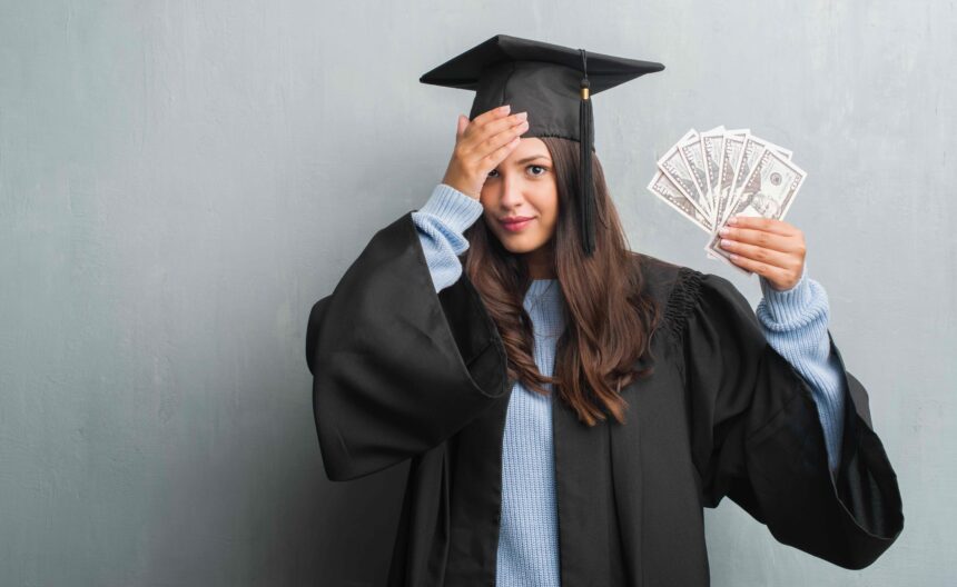 young-brunette-woman-over-grunge-grey-wall-wearing-2025-10-13-06-51-05-utc A woman in graduation robes looks stressed about money