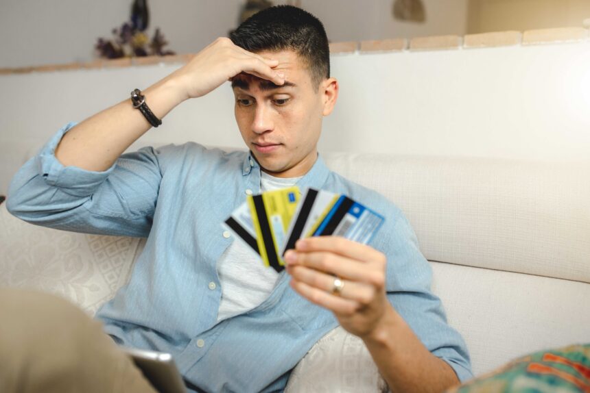 young-hispanic-man-with-a-worried-face-doing-onlin-2025-02-02-15-02-14-utc A shallow focus of a young Hispanic man with a worried face sitting on the sofa at home holding many credit cards